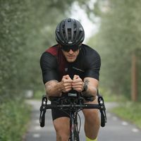 Triatleta con trisuit personalizzata su bici da cronometro in posizione aerodinamica su strada stretta