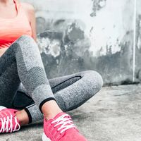 Close-up of a female athlete wearing a colourful sports top with seamless leggings and bright pink running shoes against a raw concrete background.