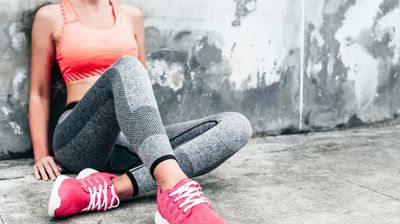Close-up of a female athlete wearing a colourful sports top with seamless leggings and bright pink running shoes against a raw concrete background.