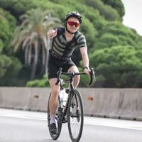 Triatleta con trisuit personalizzata in bici da corsa che fa il pollice in su su strada aperta