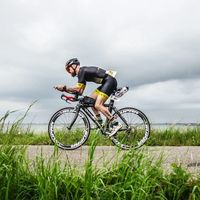 Triatleta con trisuit personalizzata su bici da cronometro in posizione aerodinamica su strada costiera